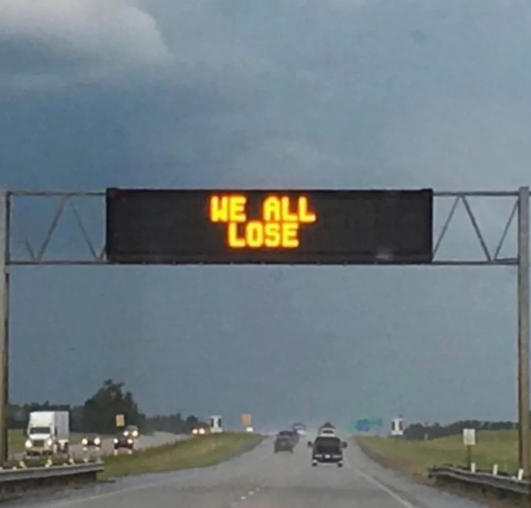 Highway sign reading WE ALL LOSE